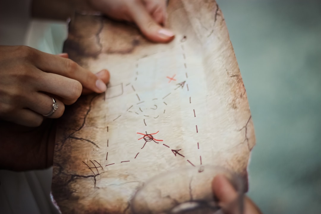 Nahaufnahme von Händen, die eine antik wirkende Schatzkarte halten und darauf zeigen. Die Karte zeigt eine Route mit gestrichelten Linien, markierten Punkten und einem großen X, das das Ziel symbolisiert. Dieses Bild passt zum Abschnitt über die Schnitzeljagd im Blog-Beitrag, da es die zentrale Idee der Schatzsuche und des Entdeckens visuellen darstellt. Es betont die Interaktivität und den Spaß an der Schnitzeljagd, bei der Teams zusammenarbeiten, Rätsel lösen und nach versteckten Hinweisen suchen, um das Ziel zu erreichen.