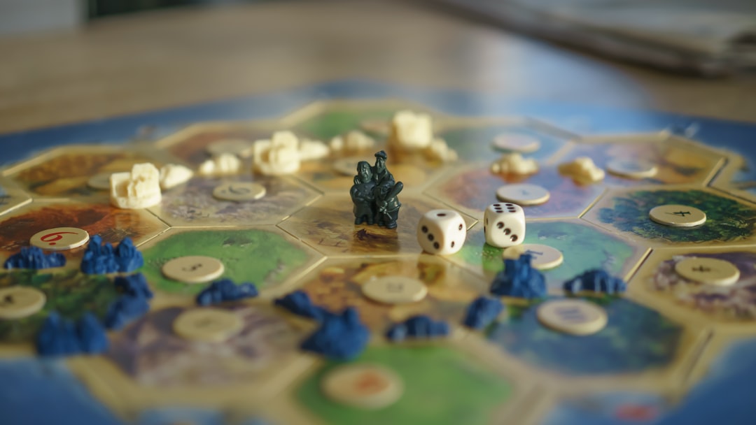 Das Bild zeigt ein Brettspiel, das auf einem Tisch aufgebaut ist, vermutlich das Spiel Die Siedler von Catan. Auf dem Spielfeld sind hexagonale Plättchen mit verschiedenen Landschaften wie Wäldern, Feldern und Bergen zu sehen. Auf einigen Plättchen befinden sich kleine Spielfiguren, Straßen und Siedlungen. Zwei Würfel und eine schwarze Spielfigur stehen im Fokus des Bildes. Dieses Bild passt perfekt zum Abschnitt über den Spieleabend im Blog-Beitrag und illustriert die gesellige und strategische Atmosphäre eines solchen Abends. Es unterstreicht die Aspekte des freundlichen Wettbewerbs, der Teamarbeit und der sozialen Interaktion, die beim gemeinsamen Spielen gefördert werden. Spieleabende bieten eine entspannte Möglichkeit, Beziehungen zu stärken und strategisches Denken zu fördern.