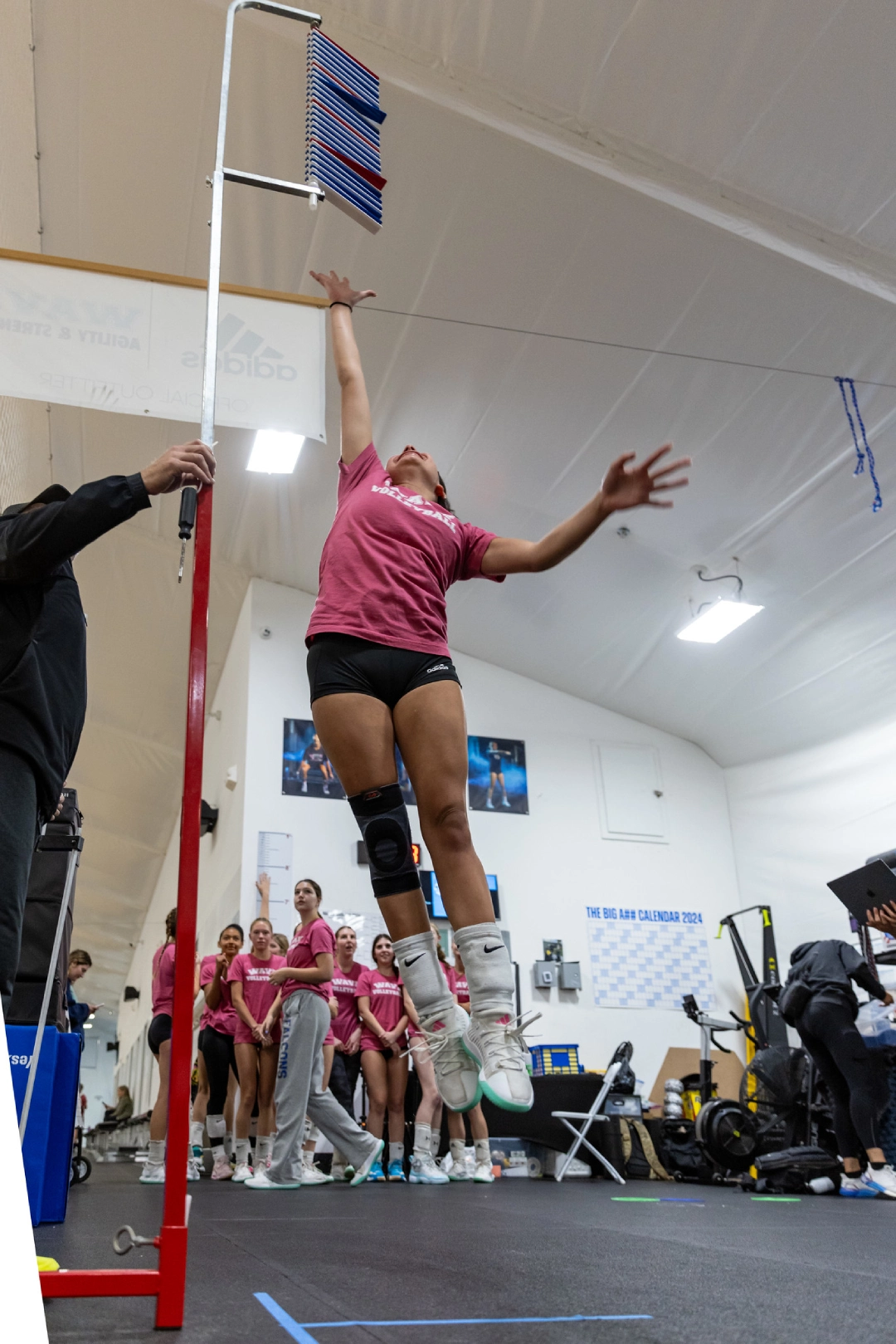 A woman jumps in the air holding a pole at Volley Strong Inc in Del Mar, CA, showcasing athleticism and energy.