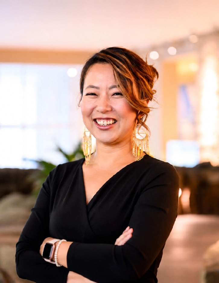 Confident executive speaker smiling with arms crossed in a warmly lit event space.