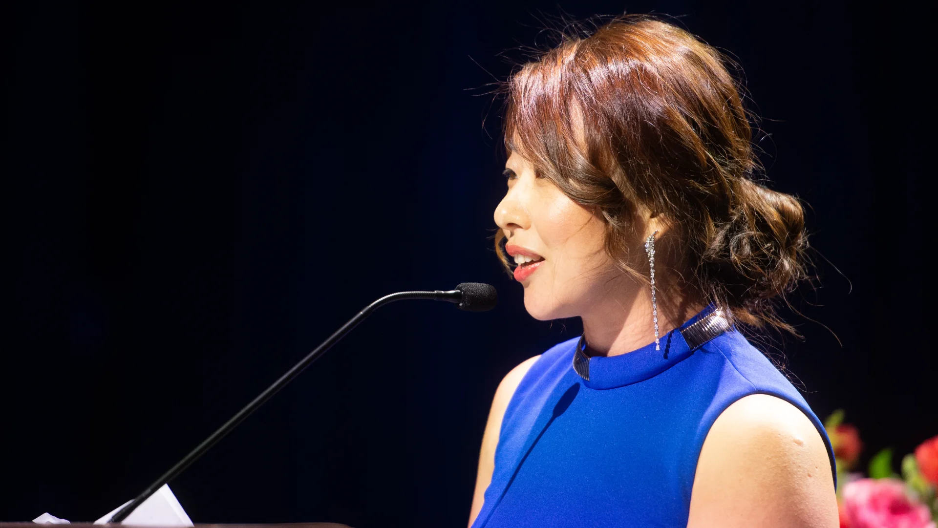 Executive speaker presenting at a podium on stage during a formal business event.