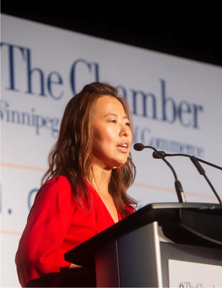 Executive speaker presenting at a business event, speaking to an audience from a podium on stage.