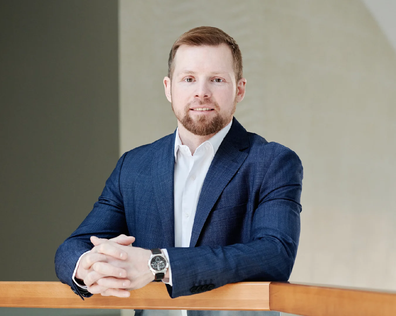 Professional man in a navy suit leaning on a railing in a bright interior space.