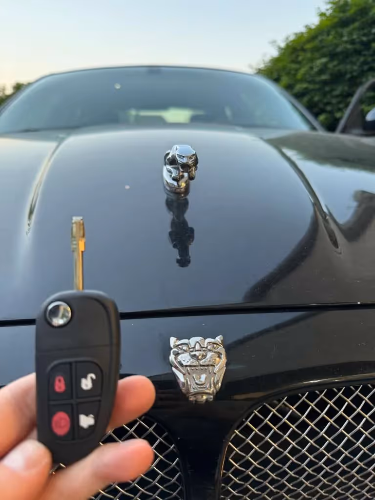 New Jaguar car key held in front of the vehicle hood emblem.