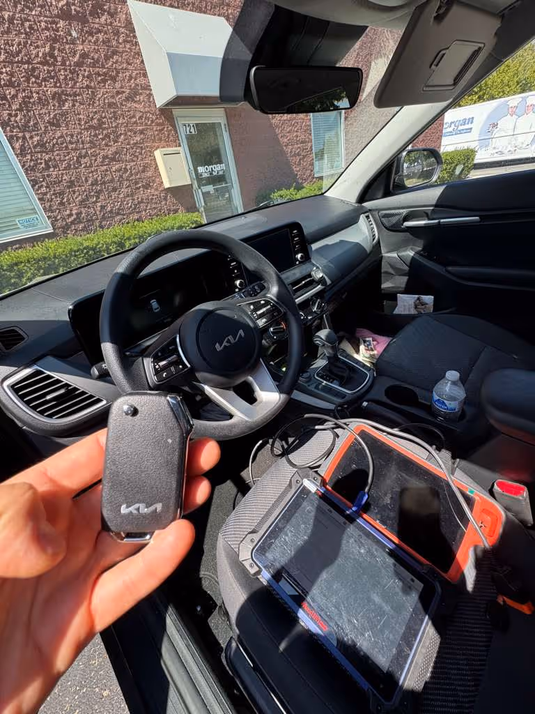 Kia car key being programmed using diagnostic equipment inside the vehicle.