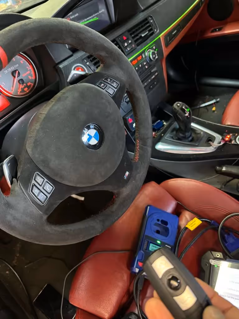 Technician programming a BMW car key inside the vehicle interior.