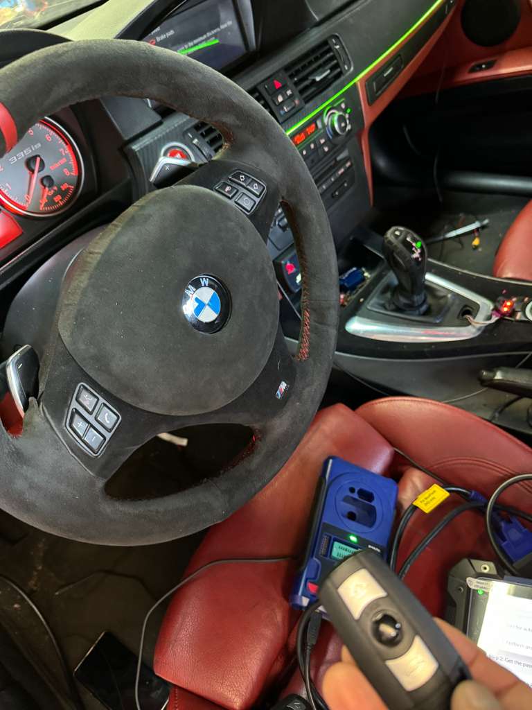 Technician programming a BMW car key inside the vehicle interior.