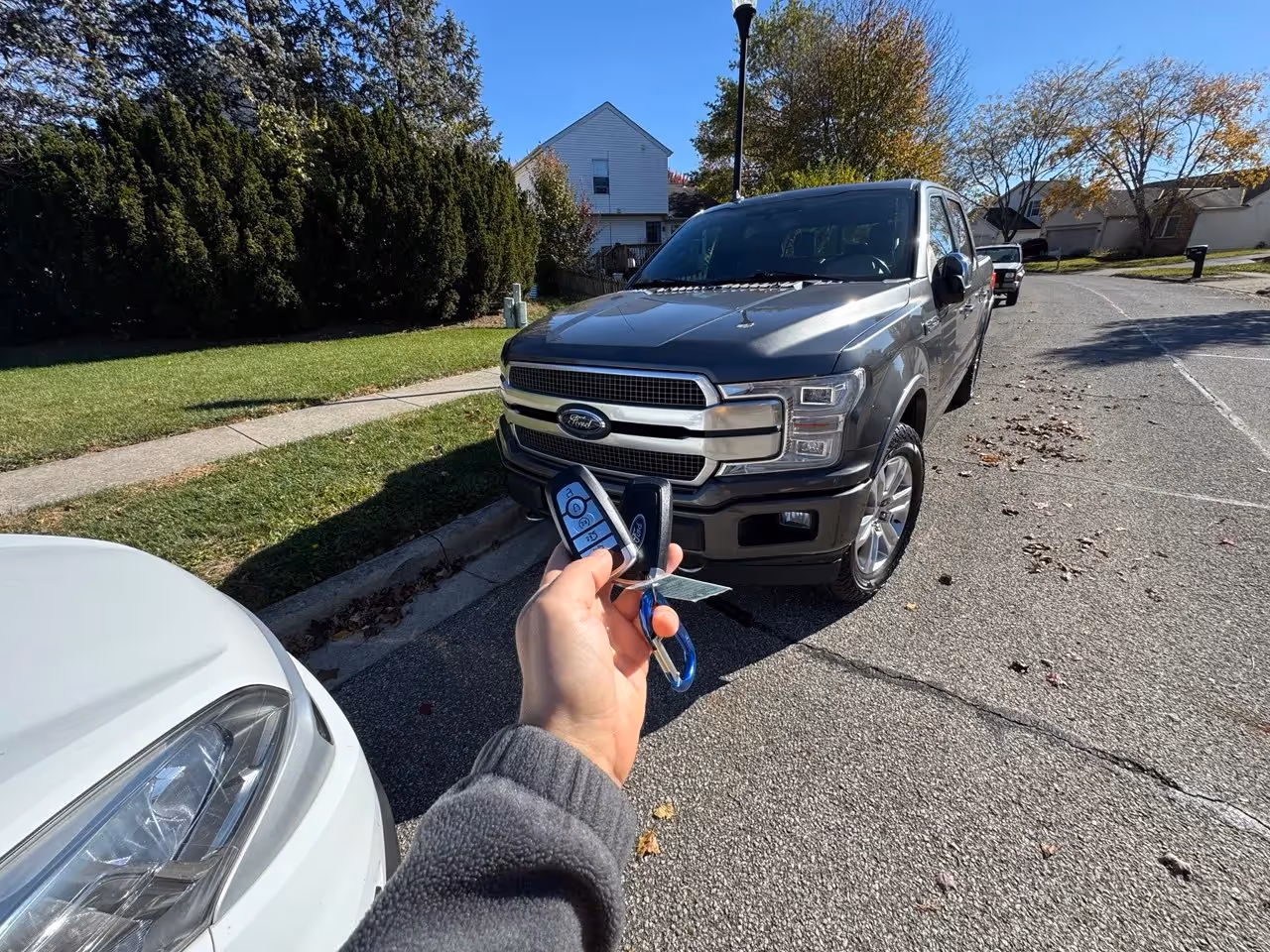 Hand holding a car key fob while standing in front of a parked vehicle.