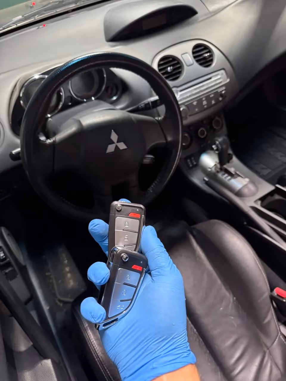 Gloved technician holding a Mitsubishi car key inside the vehicle during programming.