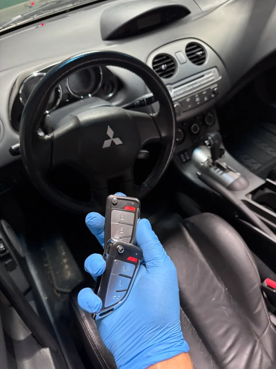 Gloved technician holding a Mitsubishi car key inside the vehicle during programming.