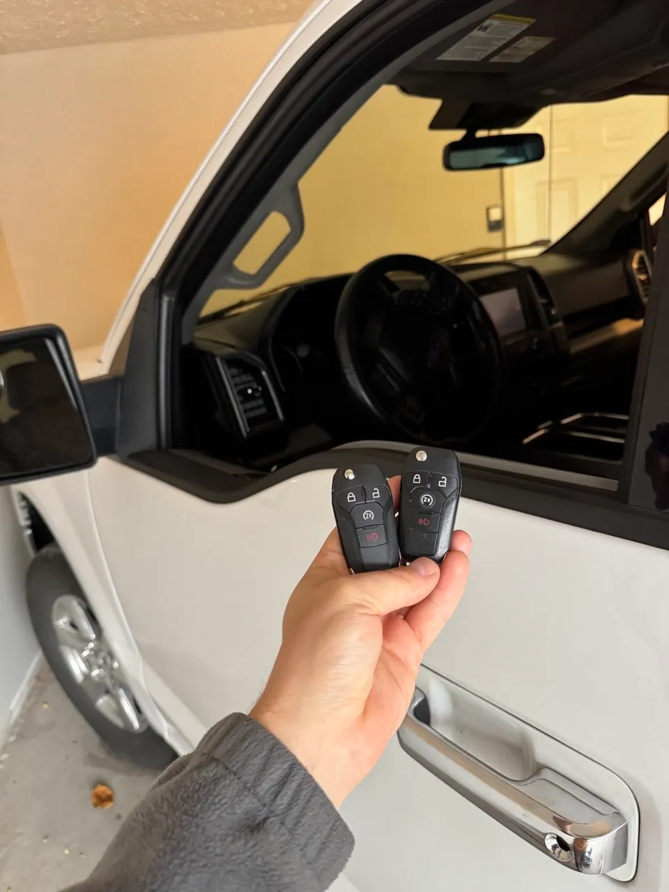 Two programmed key fobs held beside a white pickup truck’s open door