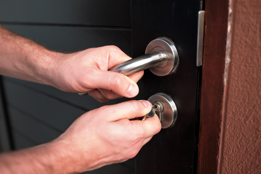 Close-up of hands unlocking a front door with a key in the deadbolt and lever handle.