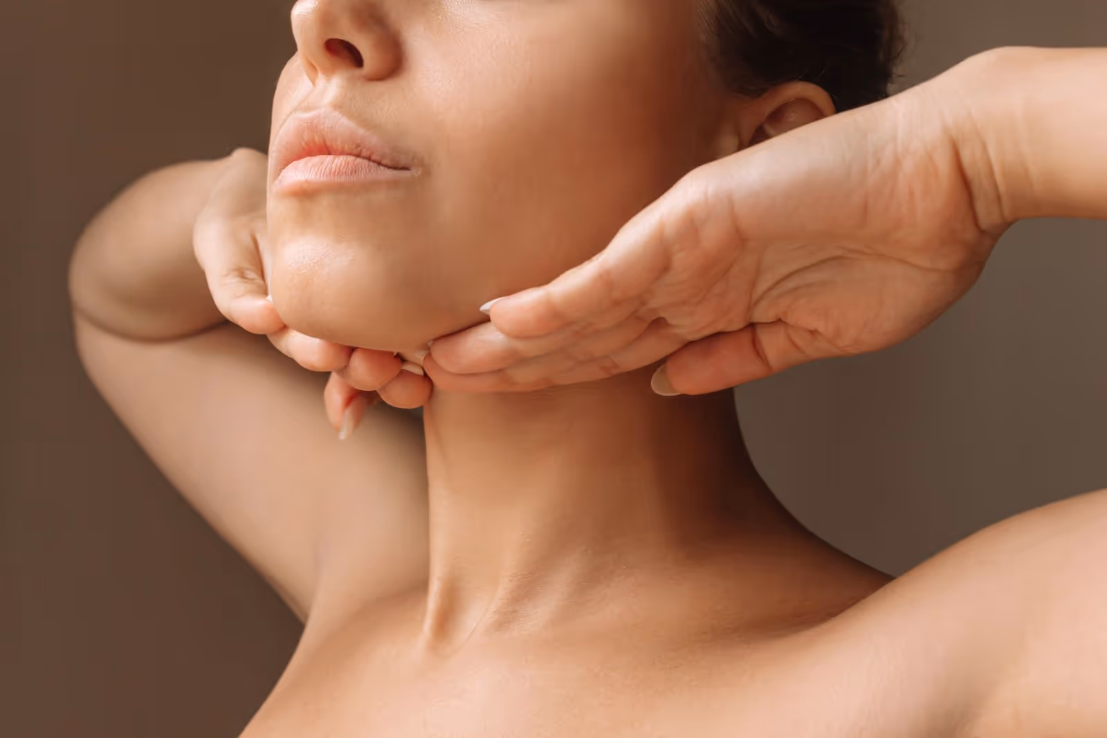 A woman is touching her neck with her hands.