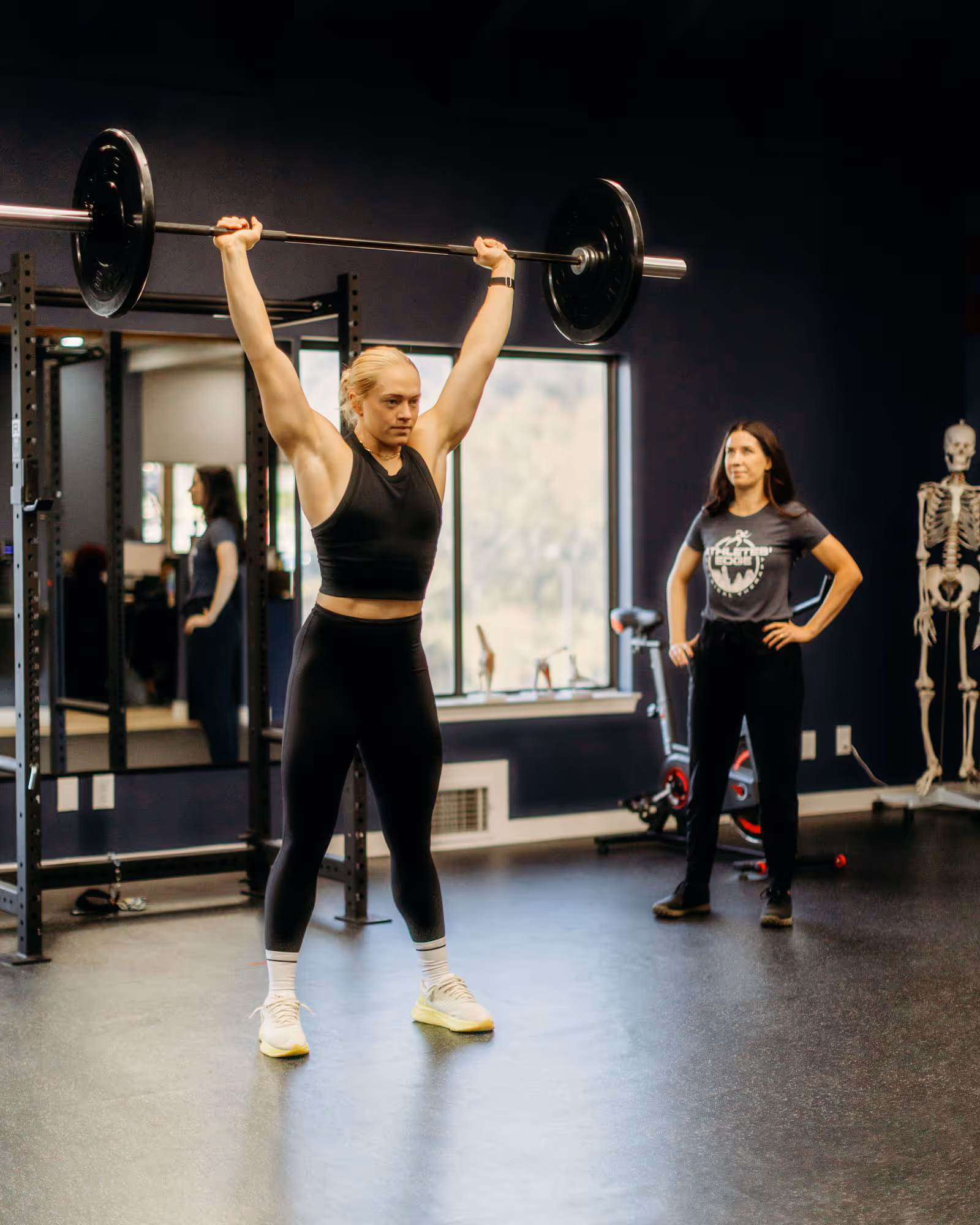 Man lifting knee while a woman catches a ball during indoor exercise session in a gym.