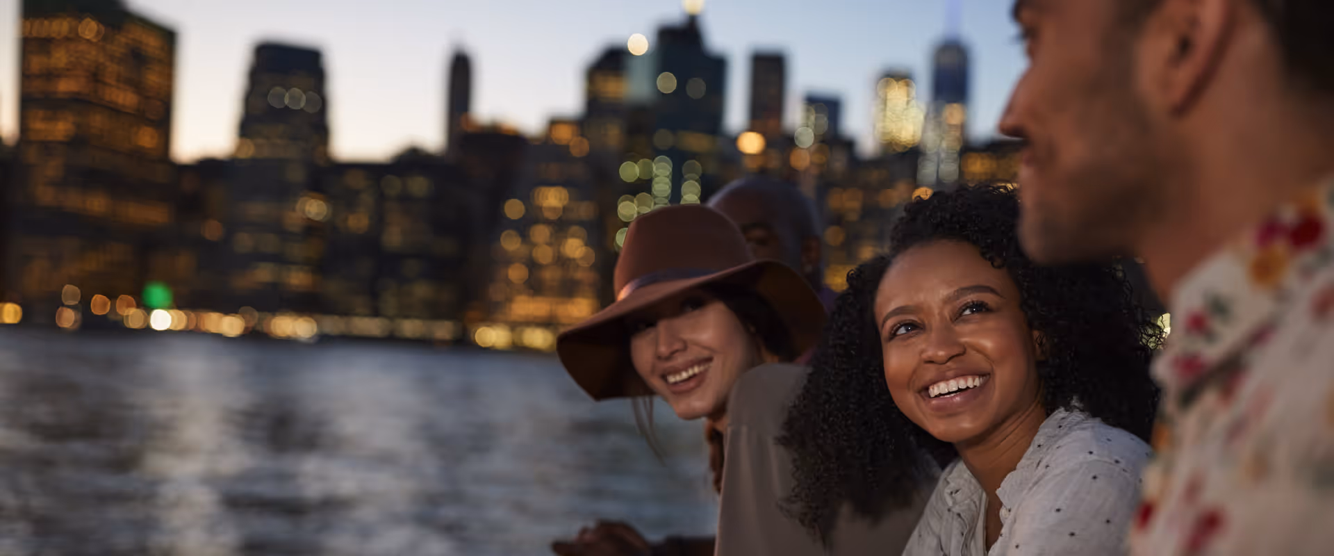 A shot of people smiling by the water across the New York City skyline.