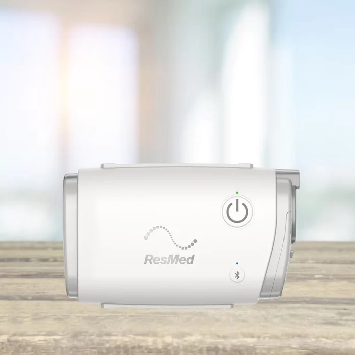 ResMed AirMini Travel Auto CPAP machine in white on a wooden surface, with power and Bluetooth indicators, for portable sleep apnea therapy

