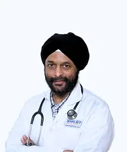 A smiling male Sikh doctor with a beard and turban, wearing a white lab coat and a stethoscope around his neck.
