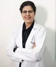 A smiling female doctor with glasses, wearing a white lab coat over a black top, standing with arms crossed.