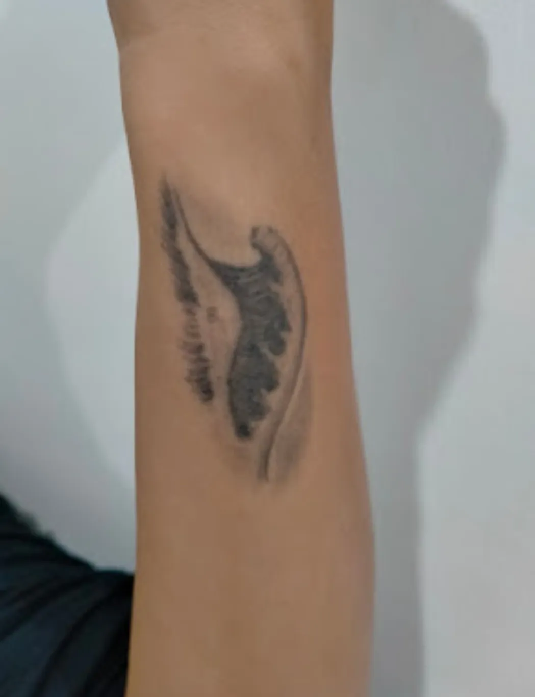 Tattoo of a black feather with an abstract design on a person's forearm.