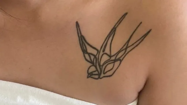 Black line-art tattoo of a swallow bird on a person's upper chest near the shoulder.