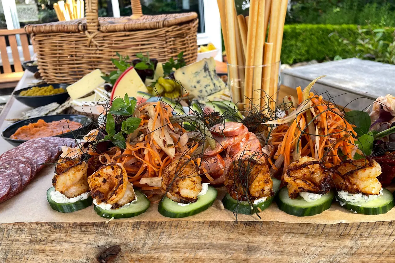Artisan charcuterie board with grilled shrimp on cucumber slices, salami, cheese wedges, dips, and breadsticks on wooden table
