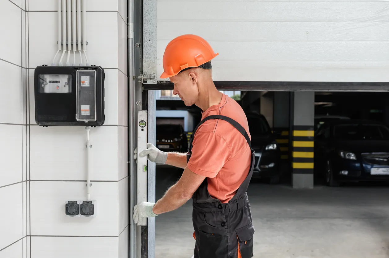 Worker in an orange hard hat and gloves adjusts a garage door.