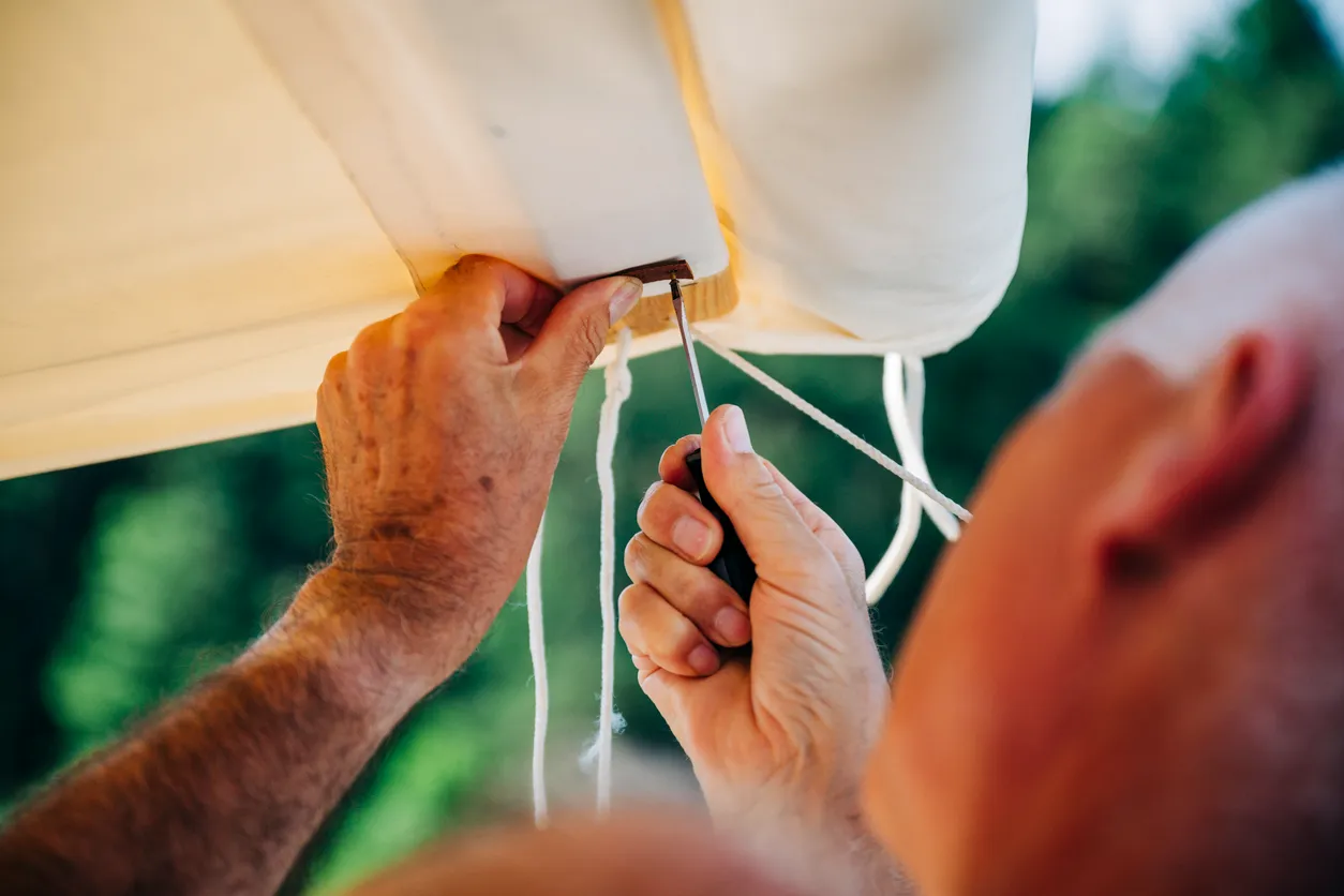 A close shot of a person's hand repairing a torn awning fabric