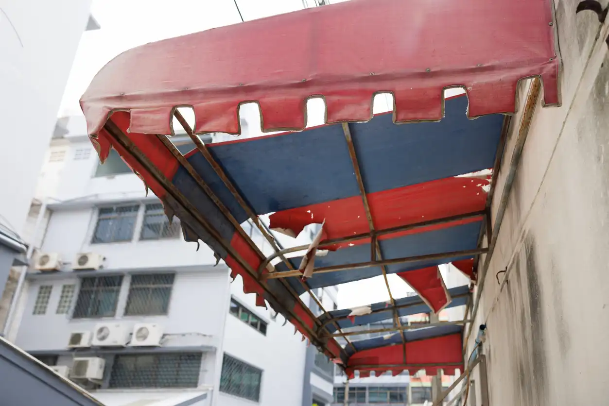 Worn red and blue striped awning with scalloped edge on urban building, damaged sections visible