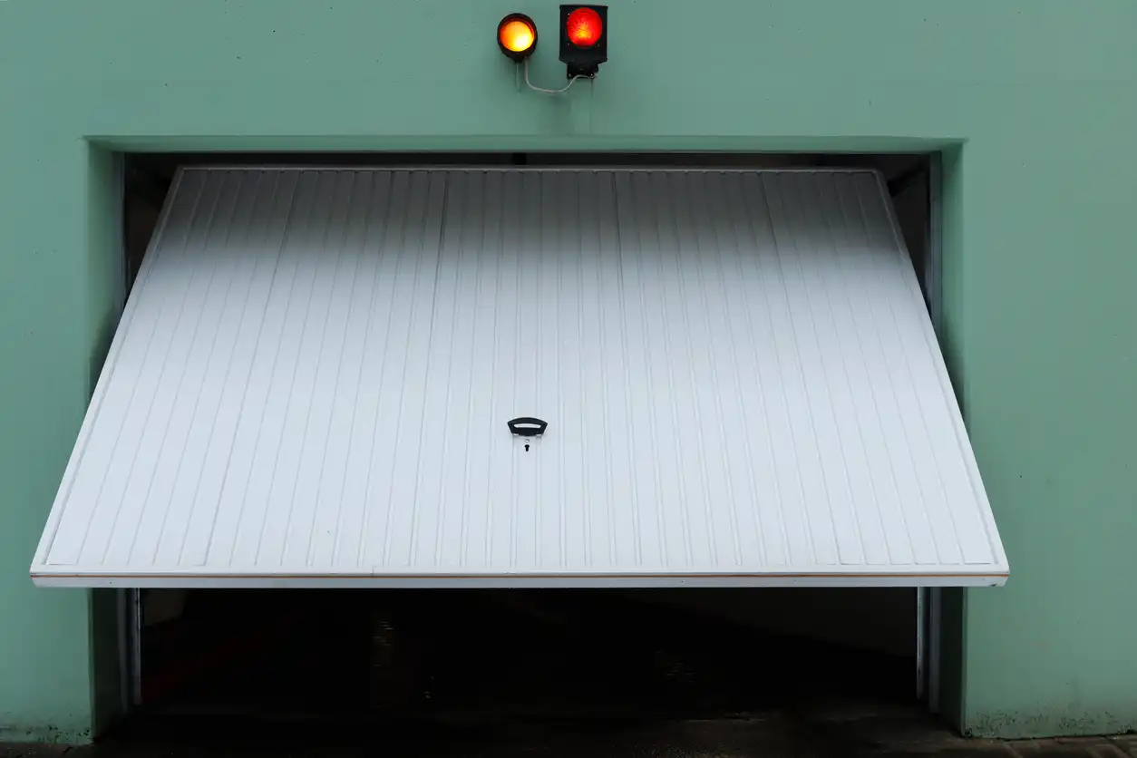 A white garage door with a handle is partially open beneath two red and orange traffic lights.
