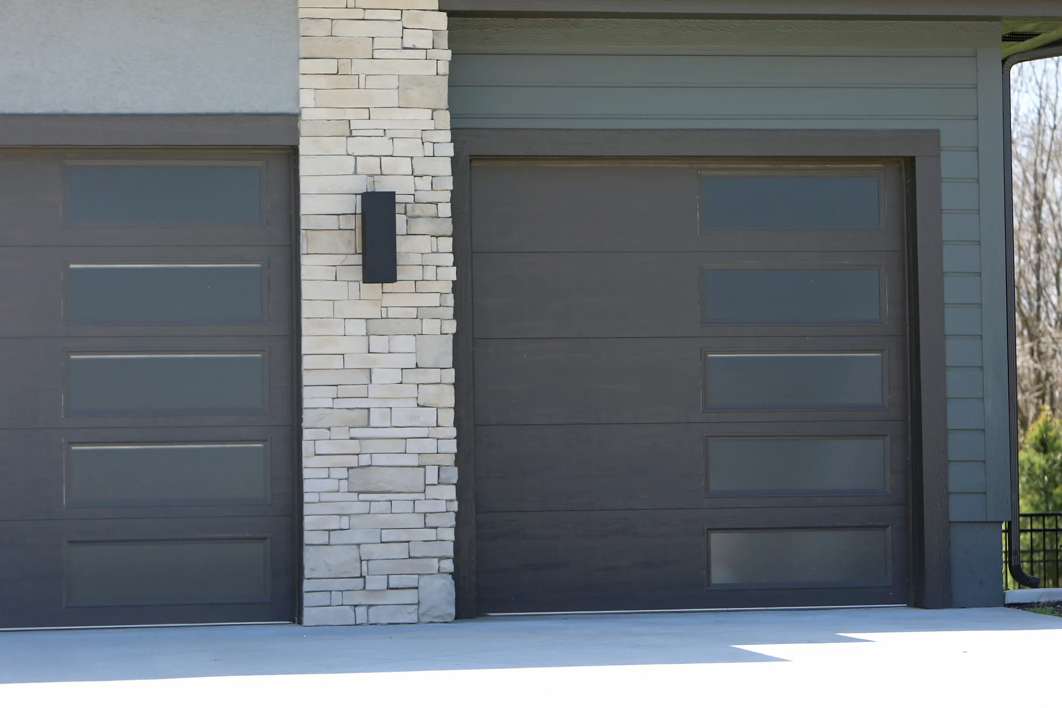 A modern, dark gray garage door with a column of four frosted glass windows on the right side.