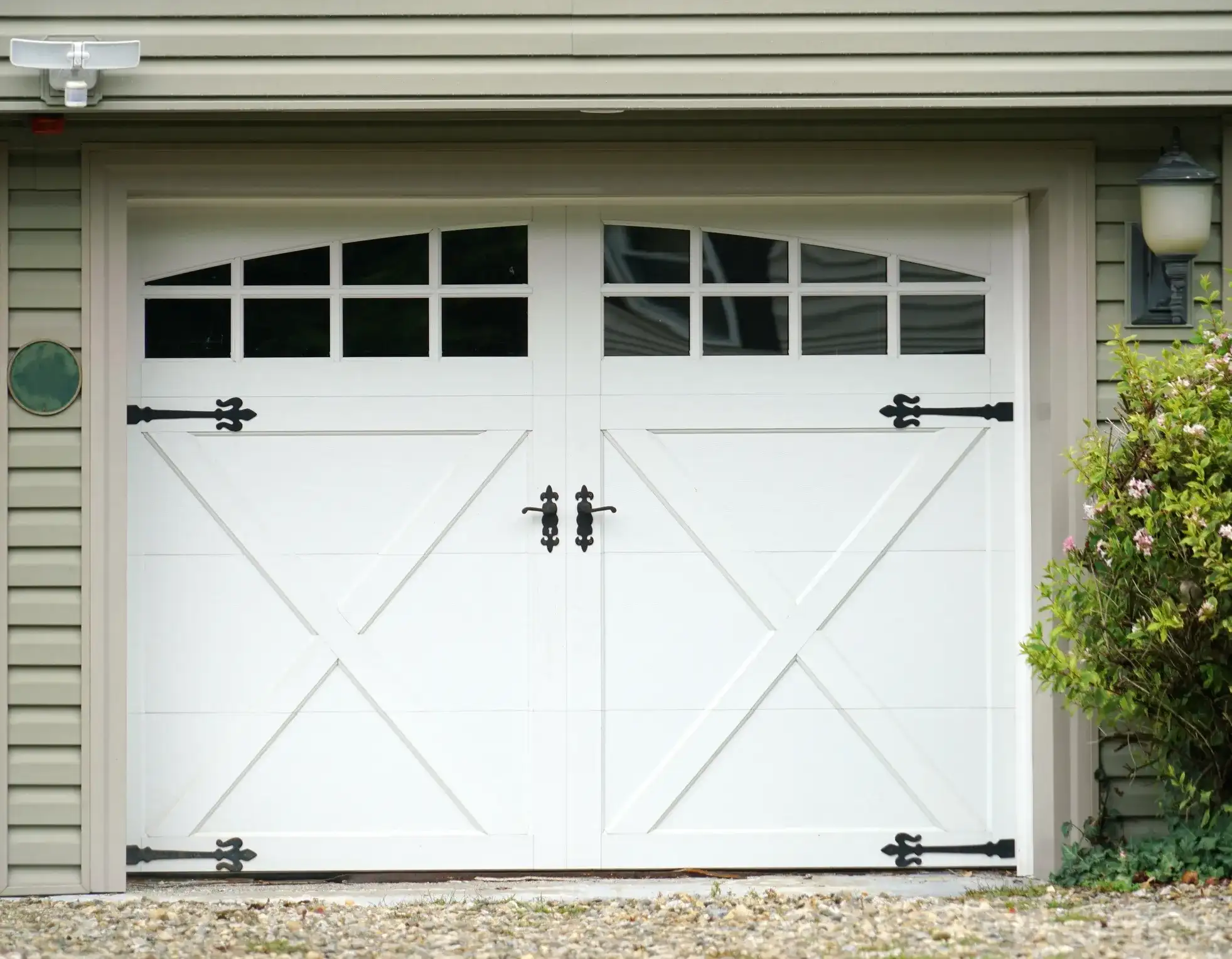 A white two-car garage door with an X-brace design and decorative black hinges, handles, and windows.