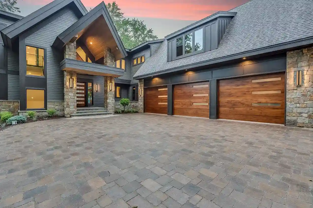 A large modern house with a stone and wood exterior, featuring three garage doors with horizontal wood panels and frosted glass strips.