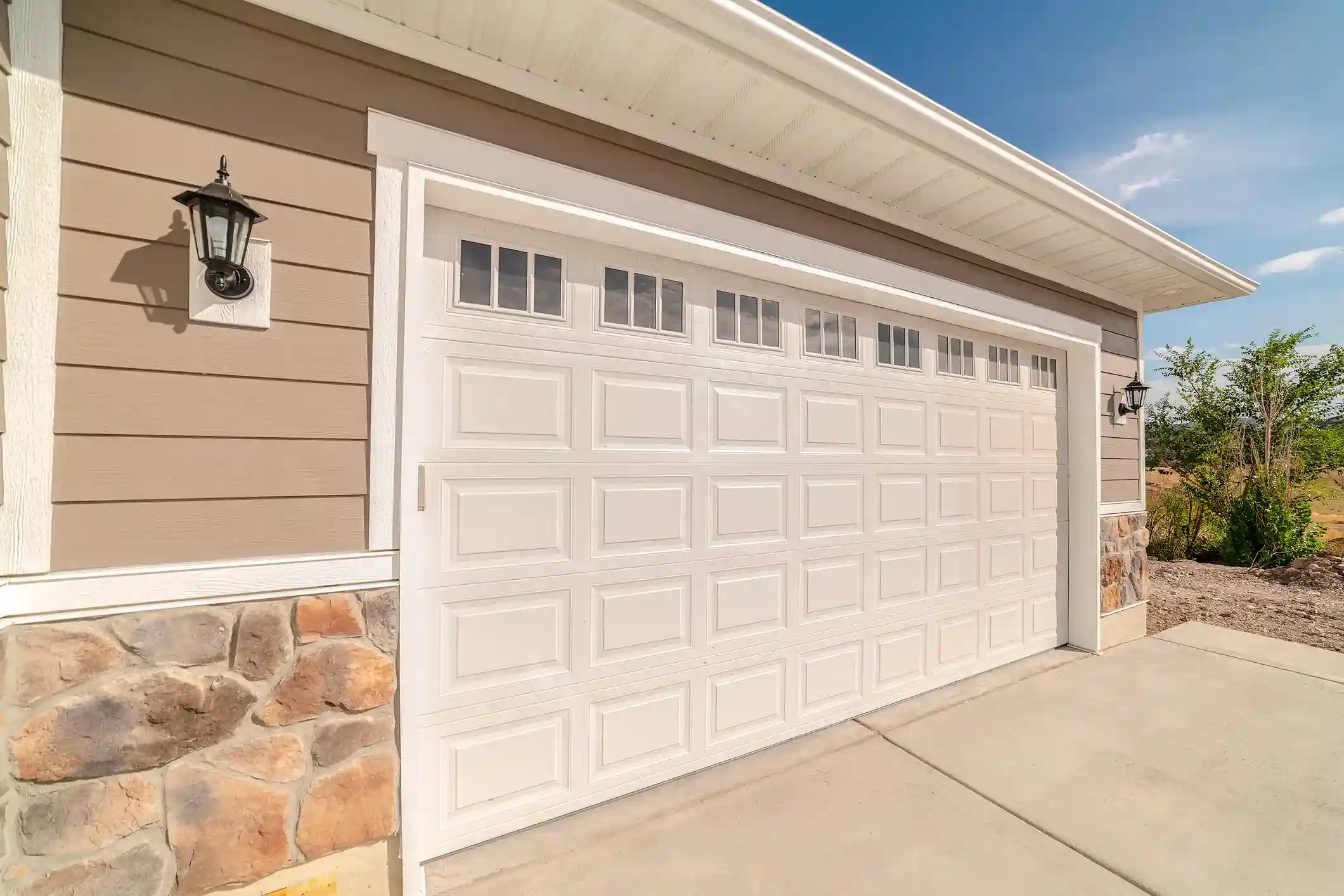 White garage door with small windows, set in a beige house with stone accents and outdoor lanterns.