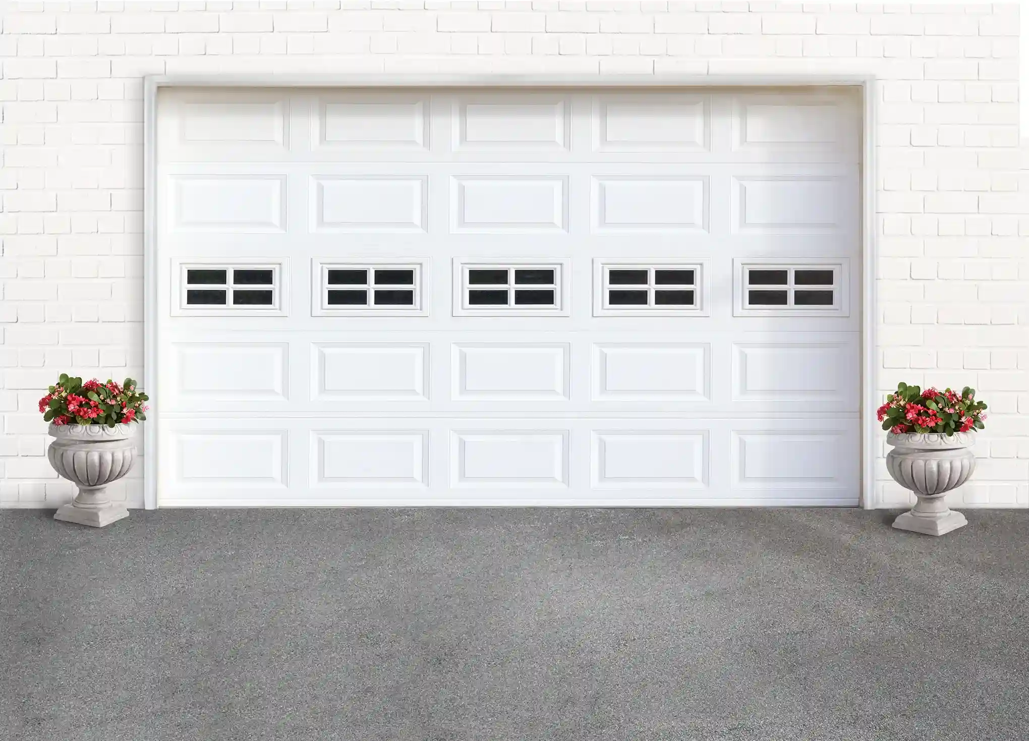 A white paneled garage door with a row of five small square windows in the middle, framed by two decorative urns with red flowers.