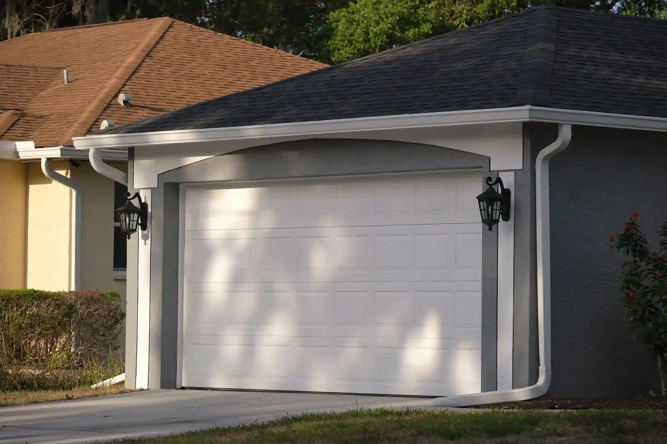 A white paneled garage door with a decorative arched frame and two black lantern lights on a gray stucco garage.
