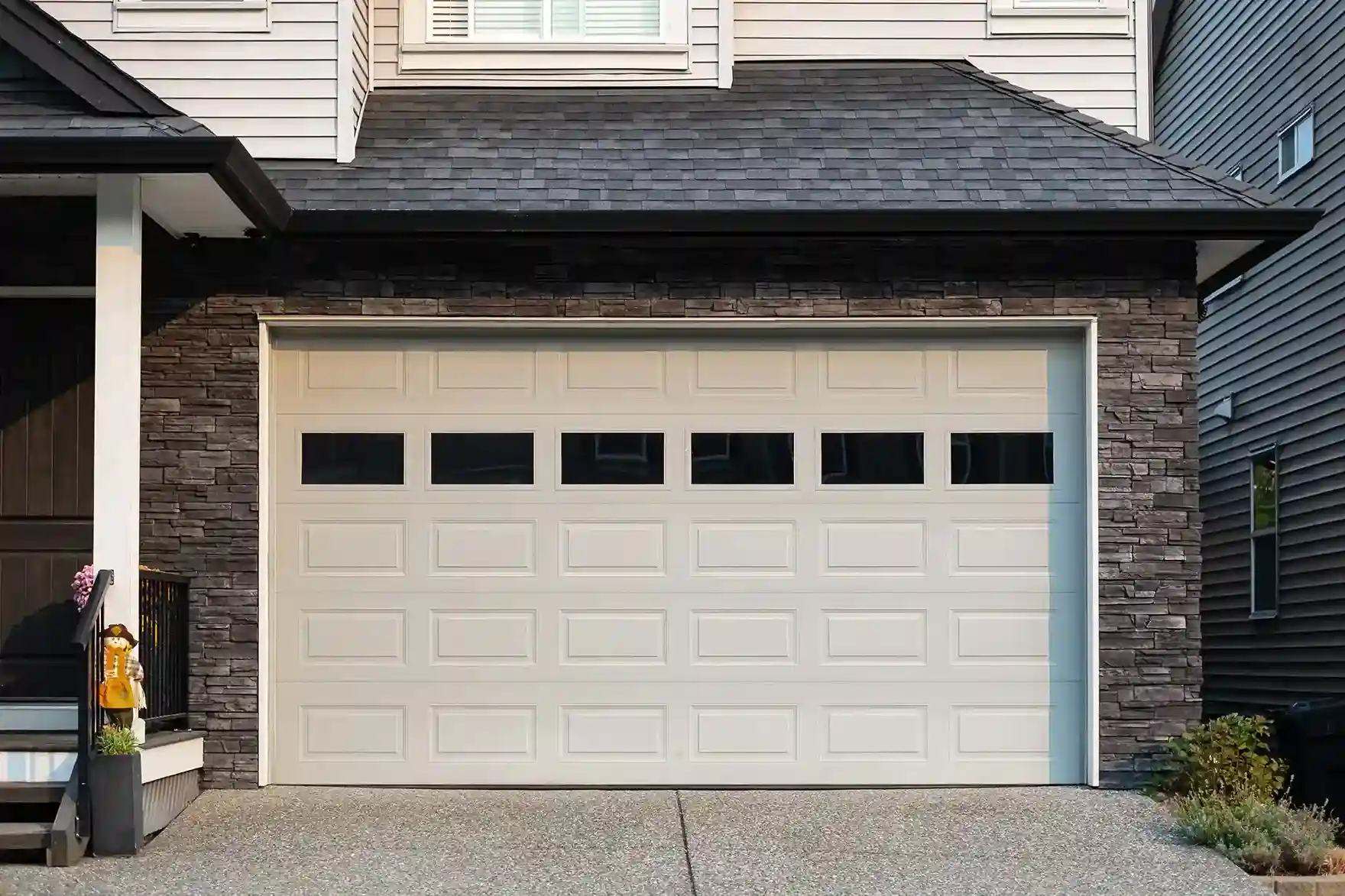 Modern house façade with a stone-accented garage featuring a white paneled door and rectangular windows,