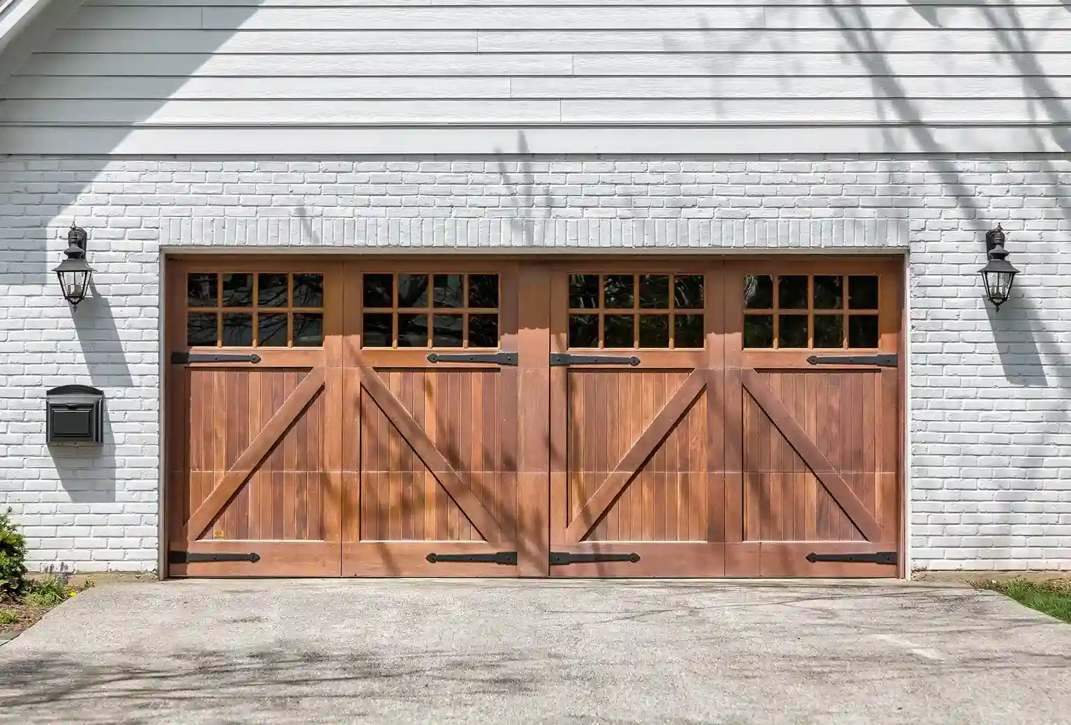 A two-car wooden garage door with an X-brace design and gridded windows on a white brick house.