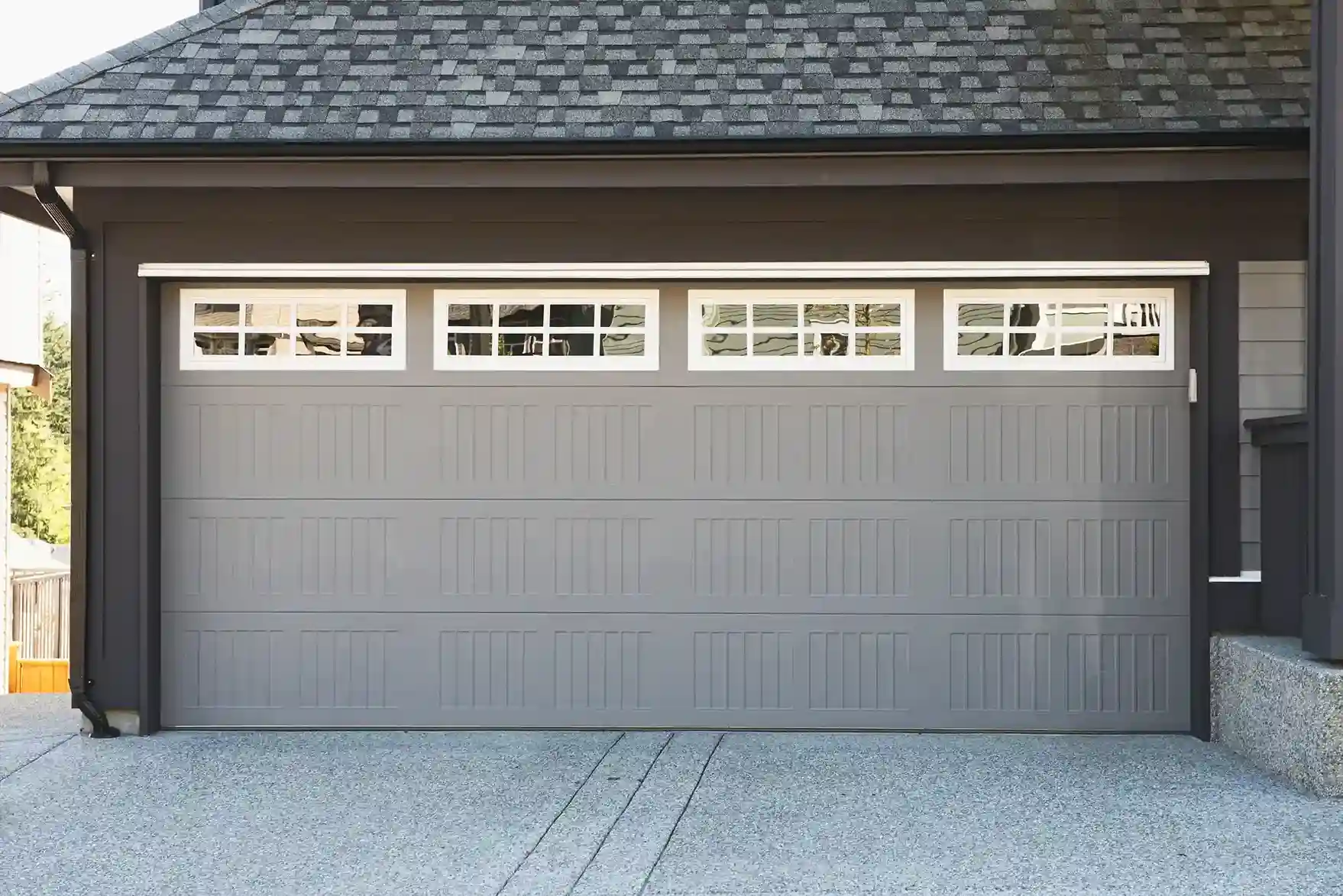 A gray paneled garage door with four white-framed windows on top, each with multiple panes.