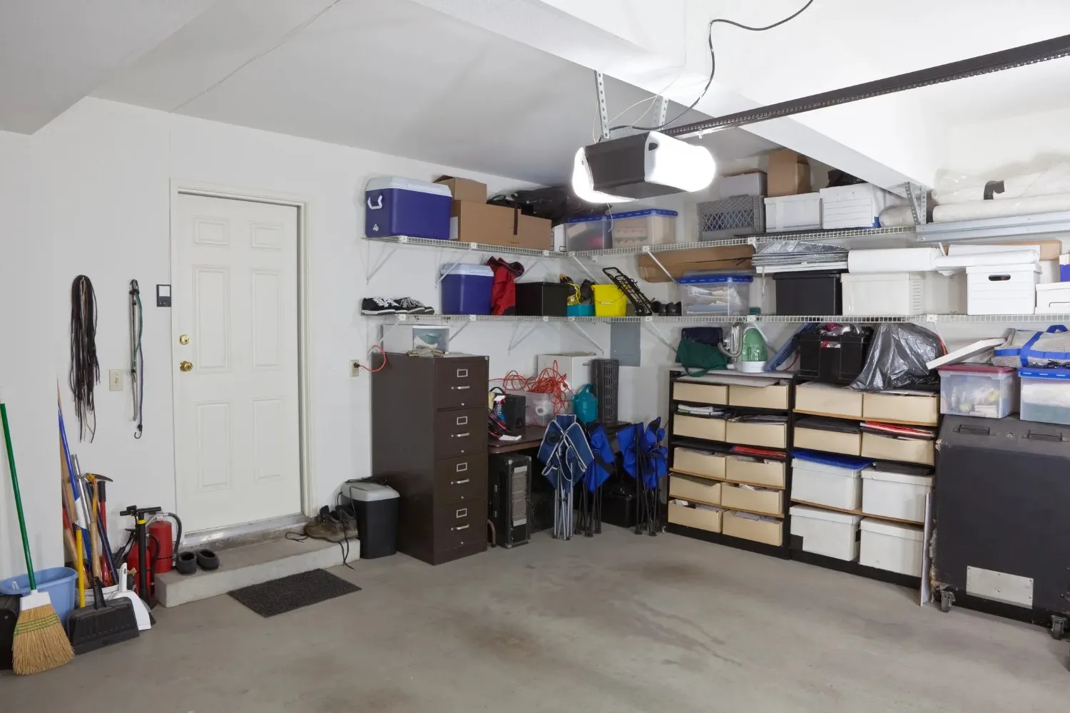 A garage interior with a mix of storage solutions, featuring metal shelving units, a filing cabinet, and a fire extinguisher near a closed white door.