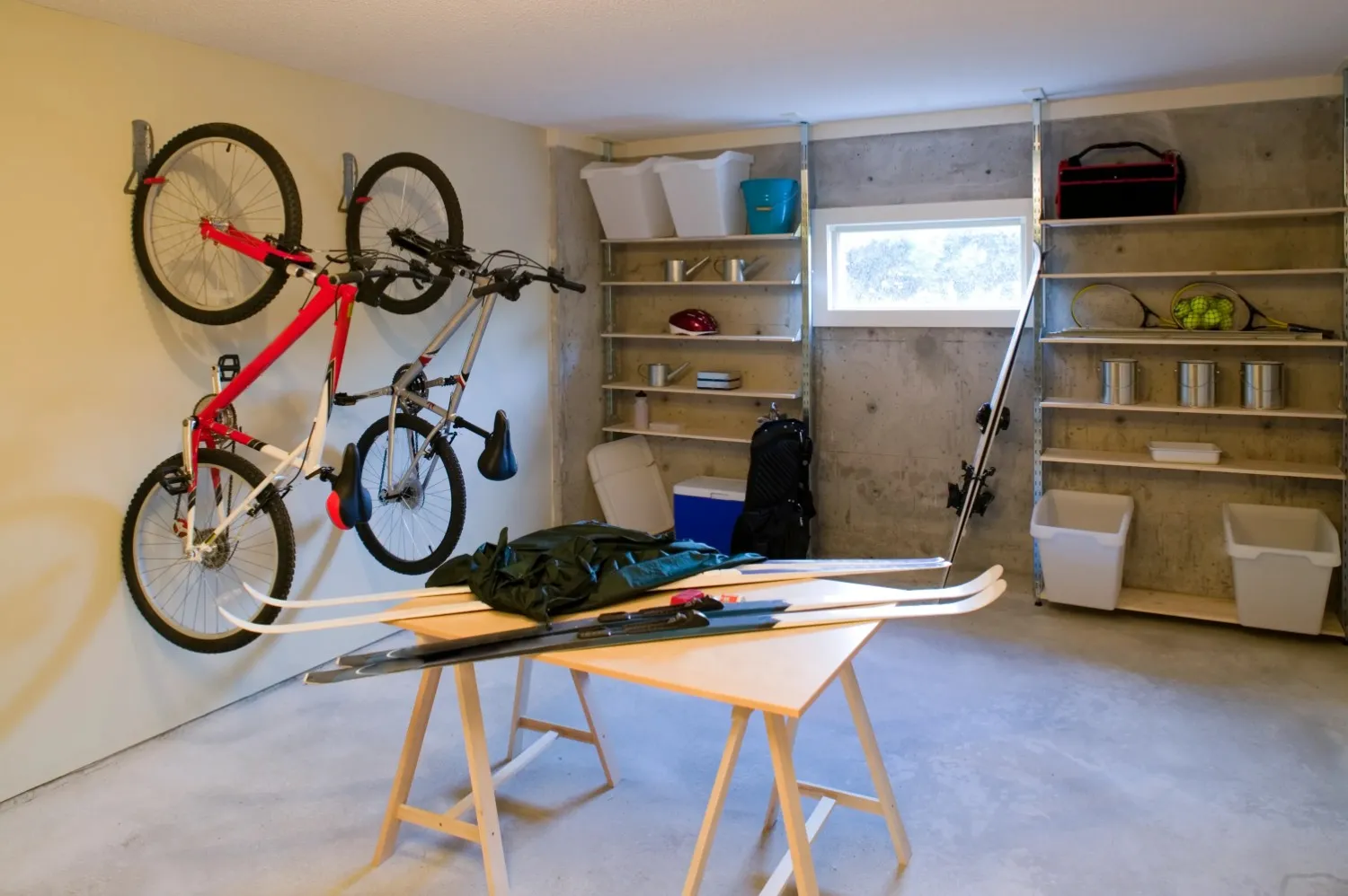 A clean garage with two bikes mounted on a wall rack and wooden shelves filled with various items, including skiing equipment on a table in the foreground.