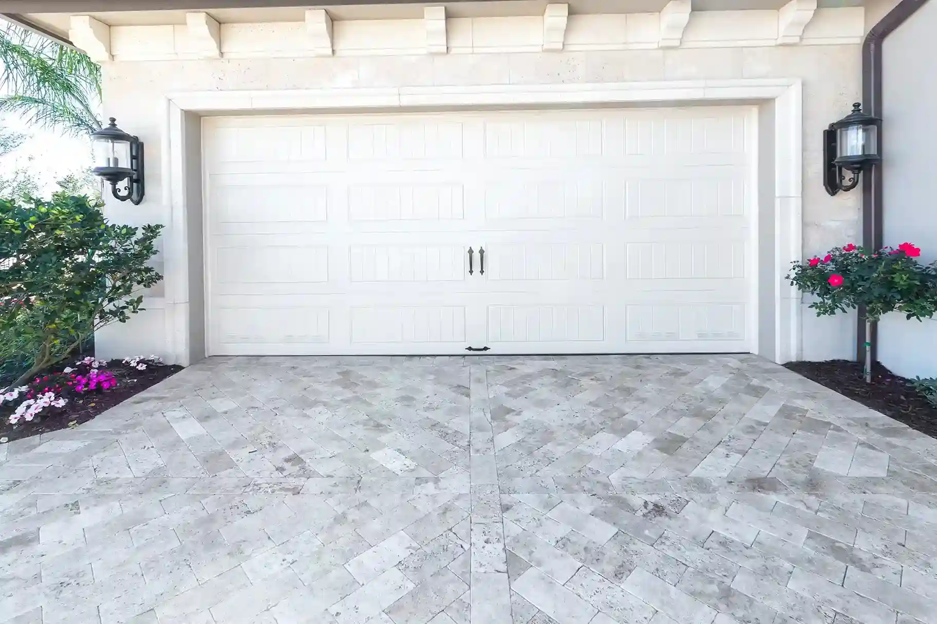 A white paneled garage door with decorative black handles and two black lantern-style lights on a light-colored stucco house.