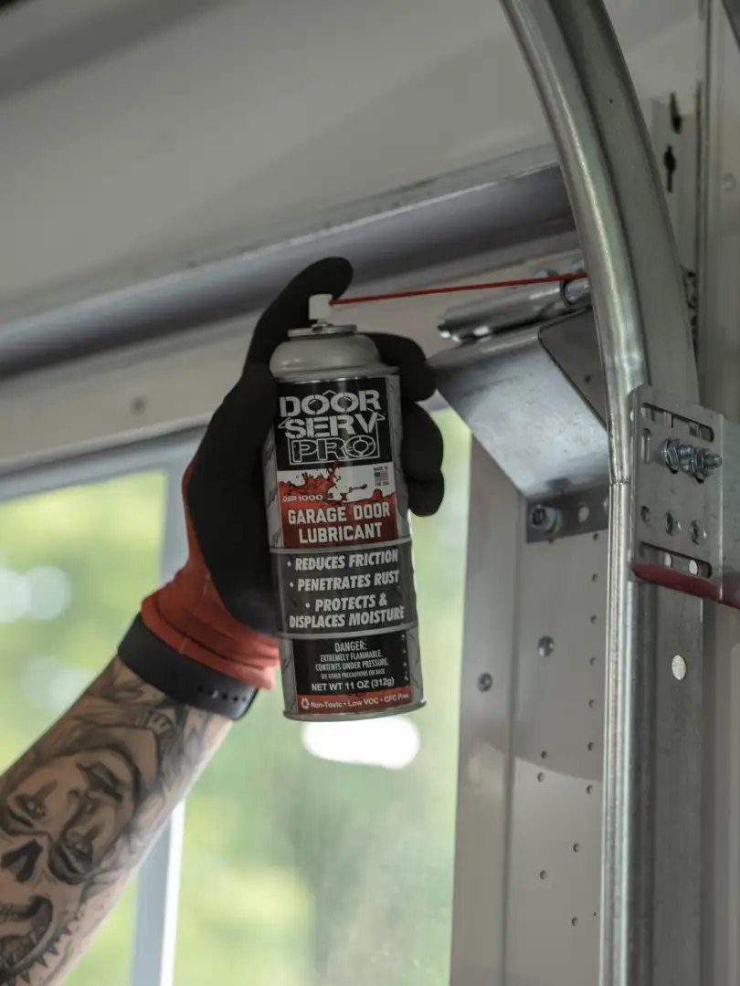 homeowner lubricating garage door rollers with silicone spray - how often should you service your garage door