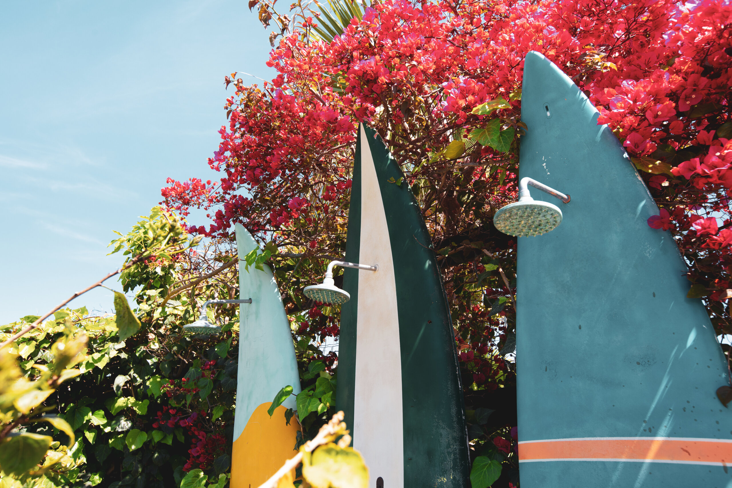 Outdoor surfboard showers in tropical garden at Floripa Surf House in Sicily with pink bougainvillea
