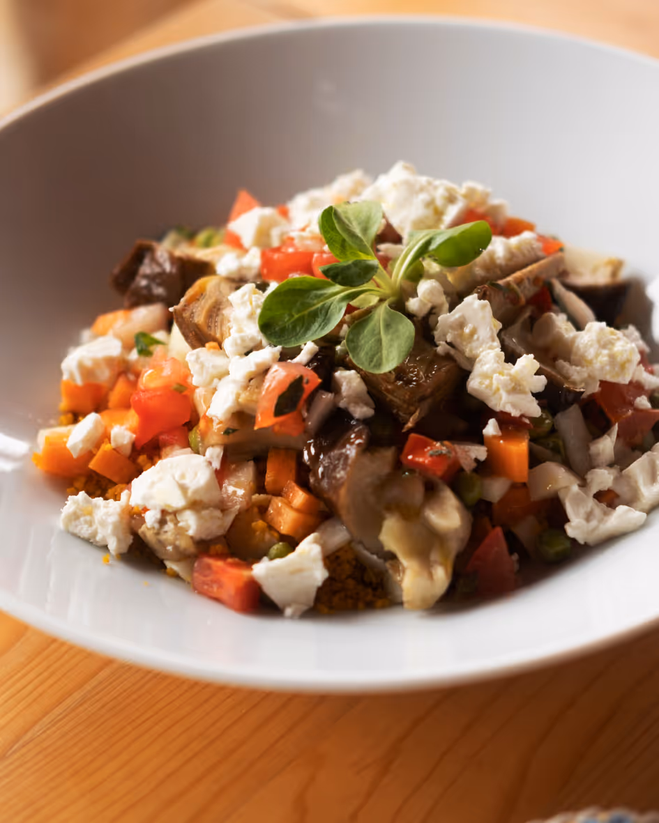 Plate of colorful vegetable salad with roasted mushrooms, diced tomatoes, carrots, peas, and crumbled white cheese garnished with fresh greens.