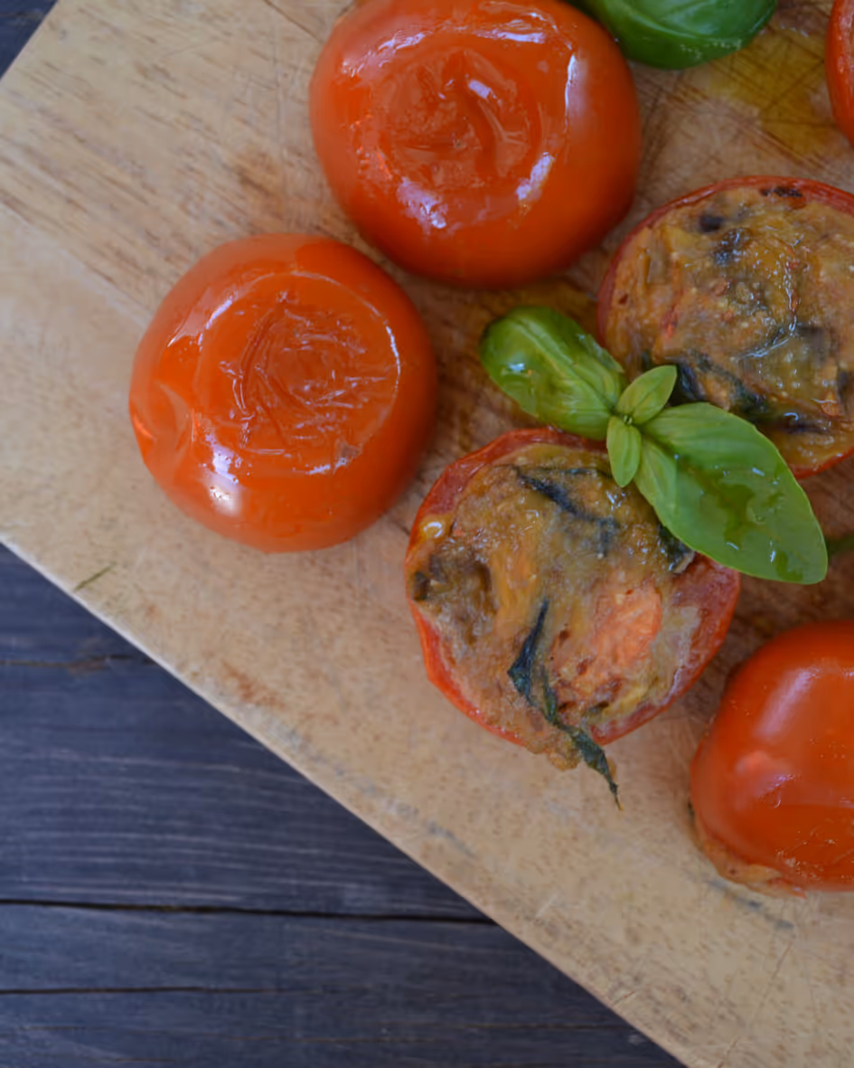 Baked stuffed tomatoes garnished with fresh basil leaves on a wooden cutting board.