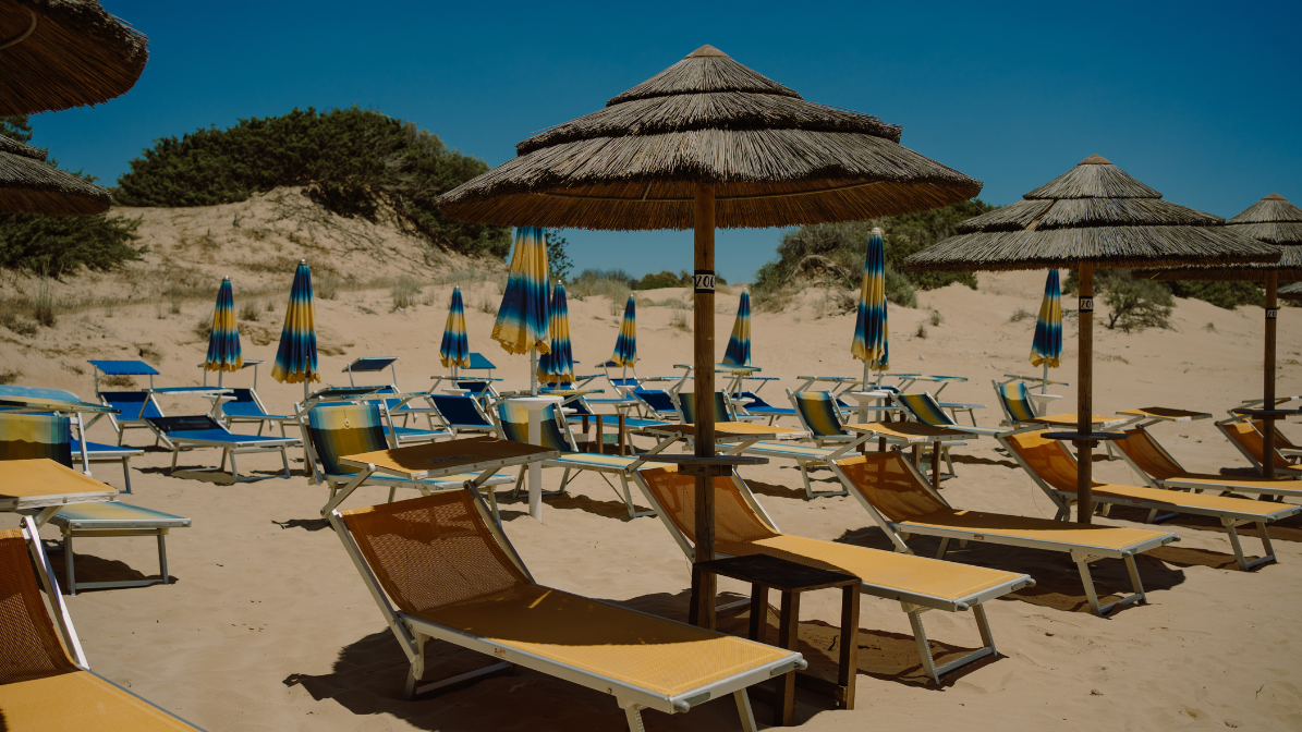 Sunbeds and parasols on the quiet sandy beach near Floripa Surf and Yoga Retreat in Sicily, offering guests private beach access and relaxation

