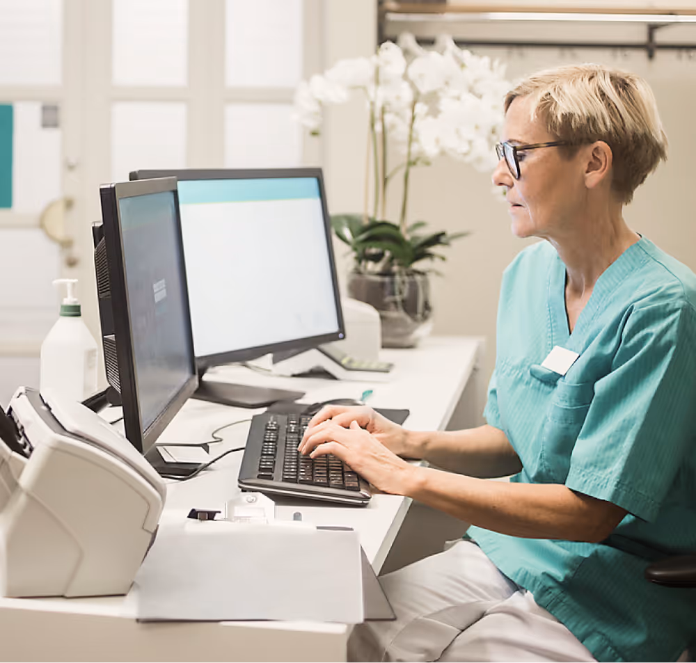 MFA mit kurzen blonden Haaren und Brille sitzt am Schreibtisch und arbeitet am Computer