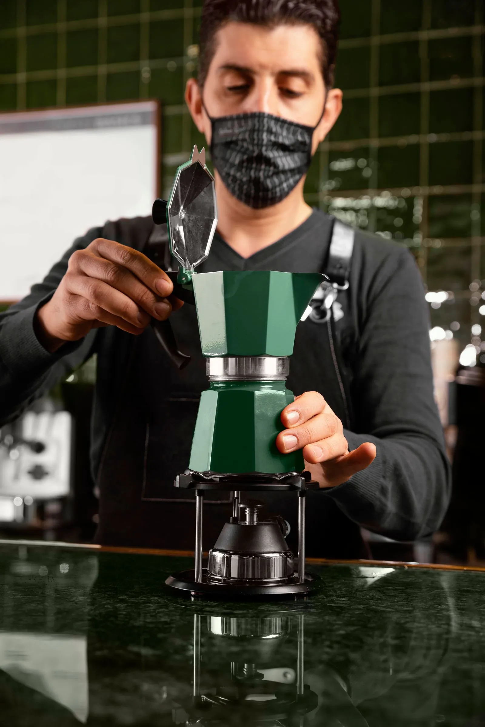Barista in mask preparing coffee with moka pot