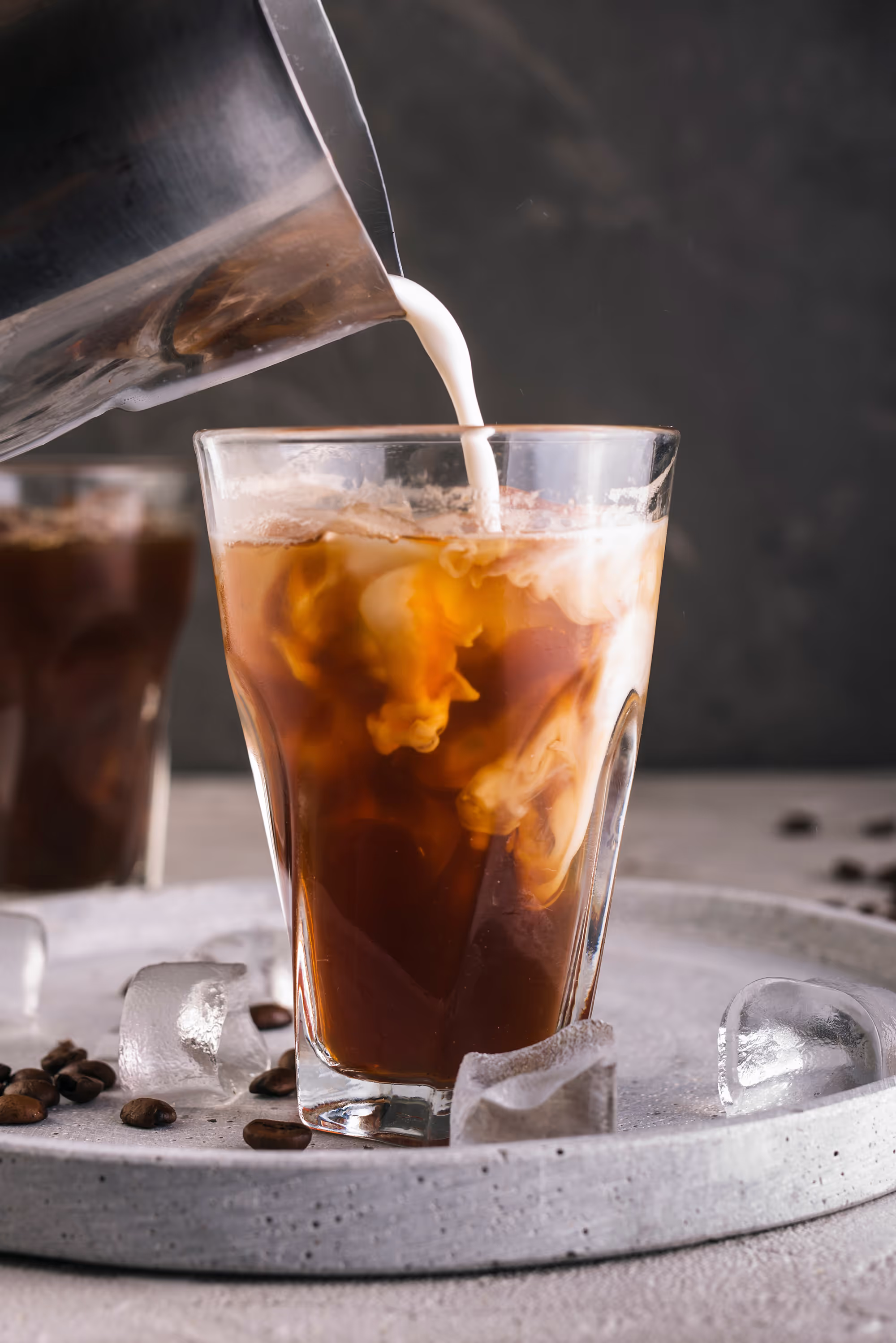 Milk swirling into iced coffee in glass