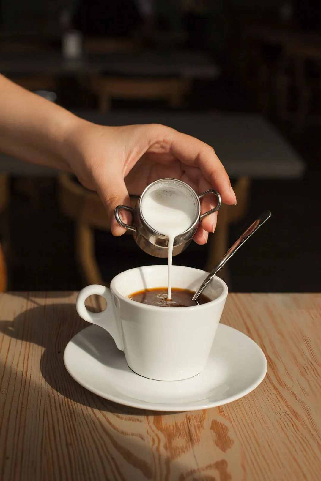 Milk being poured into black coffee in white cup